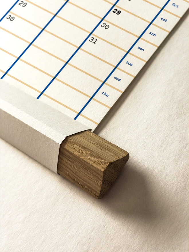 Closeup of yearly wall planner in blue on white paper, showing unique folded paper frame with oak strip insert.