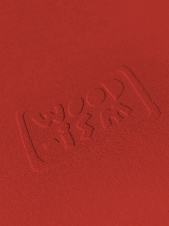 A close up of the Woodism logo embossed on the red paper