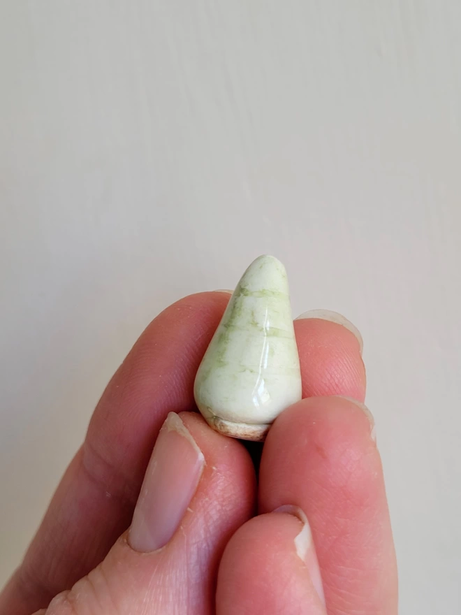 small pottery tree held in the fingertips of a hand in a pale green glaze