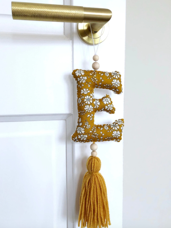 Liberty Hanging Initial Ornament. An initial hanging from a door in a floral fabric.