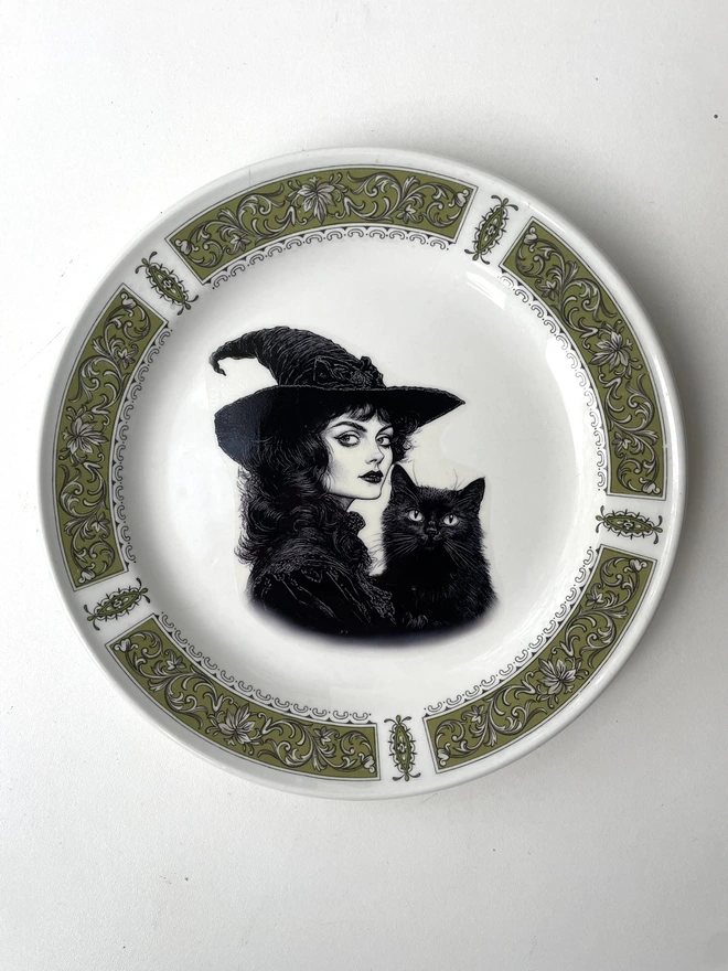 vintage plate with an ornate border, with a printed vintage illustration of a Victorian witch and her black cat in the middle 
