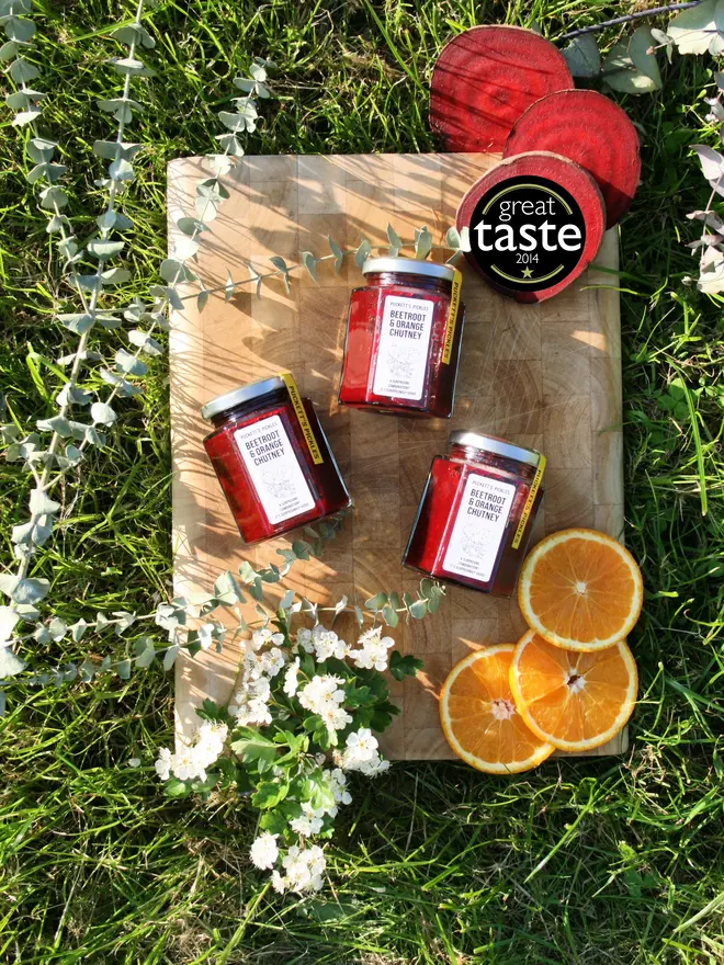 beetroot and orange chutney. jars of chutney photographed on a wooden board among grass.