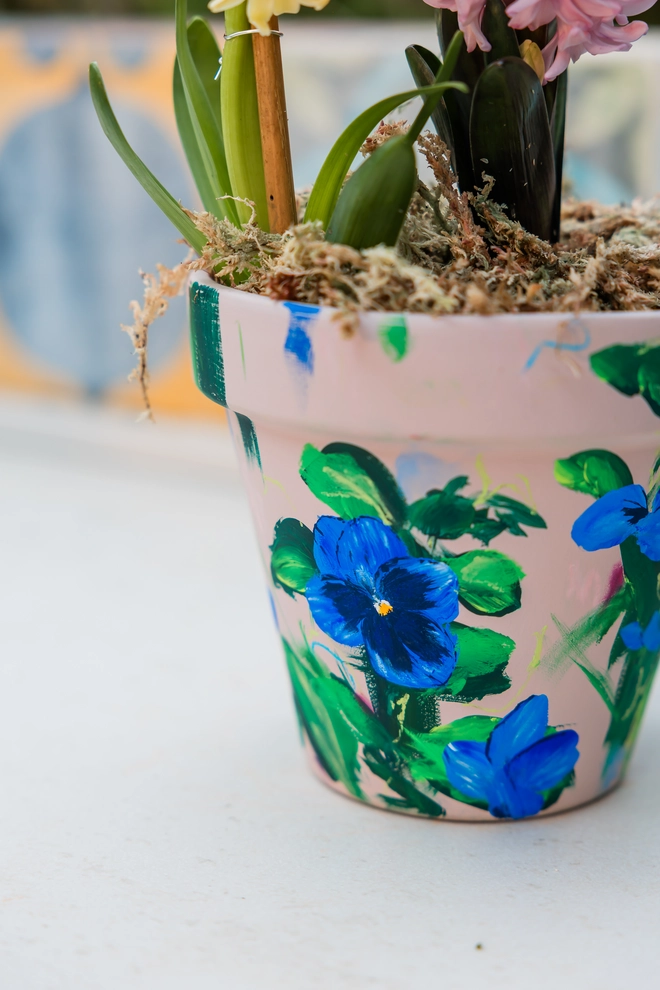 
Hand painted floral terracotta plant pot natural stone background adorned in vibrant blue blotch pansy flowers