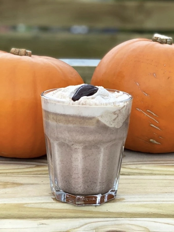 Drinking Chocolate 60% (Pack Of 200g/ 1kg), a hot chocolate sitting outside on a wooden surface next to two pumpkins. 