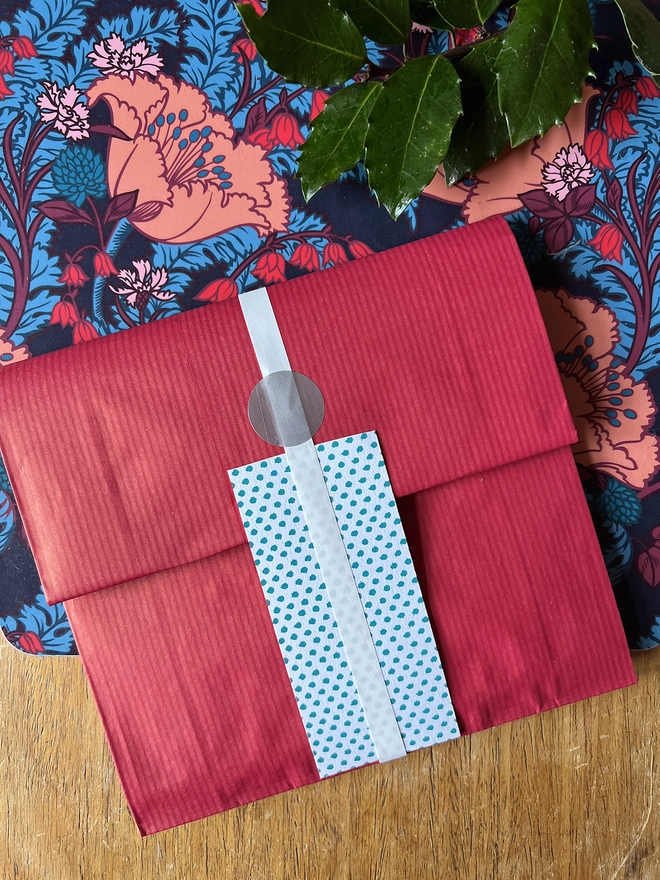 Optional gift wrap of red paper and silver ribbon, alongside christmas holly 