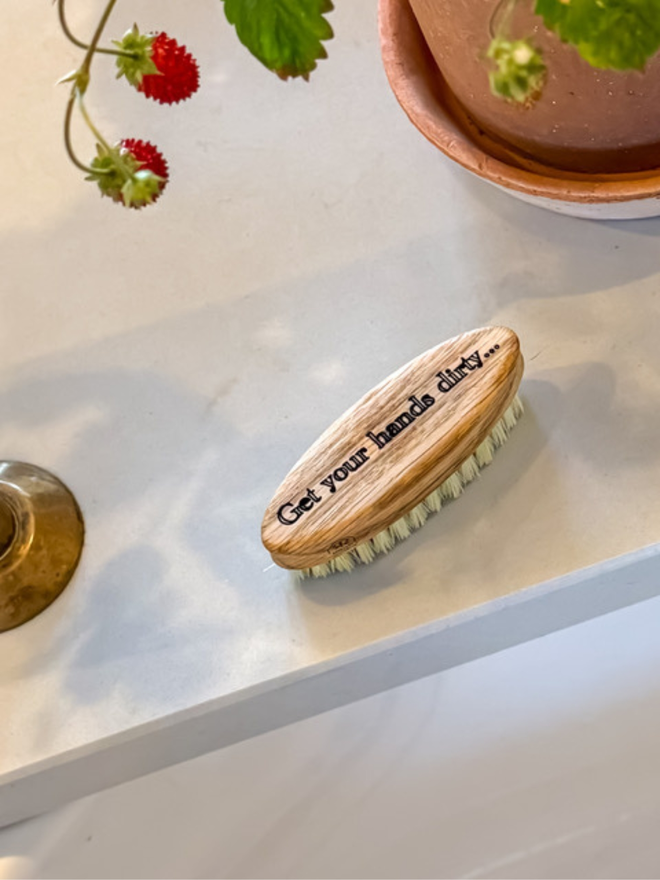 get your hands dirty oak nail brush. a wooden oak nail brush with engraving photographed on a kitchen bench.