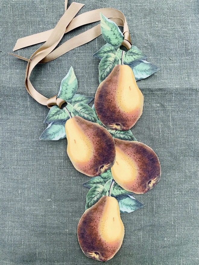 A set of four napkin ties with a botanical pear design, lying on a green linen tablecloth