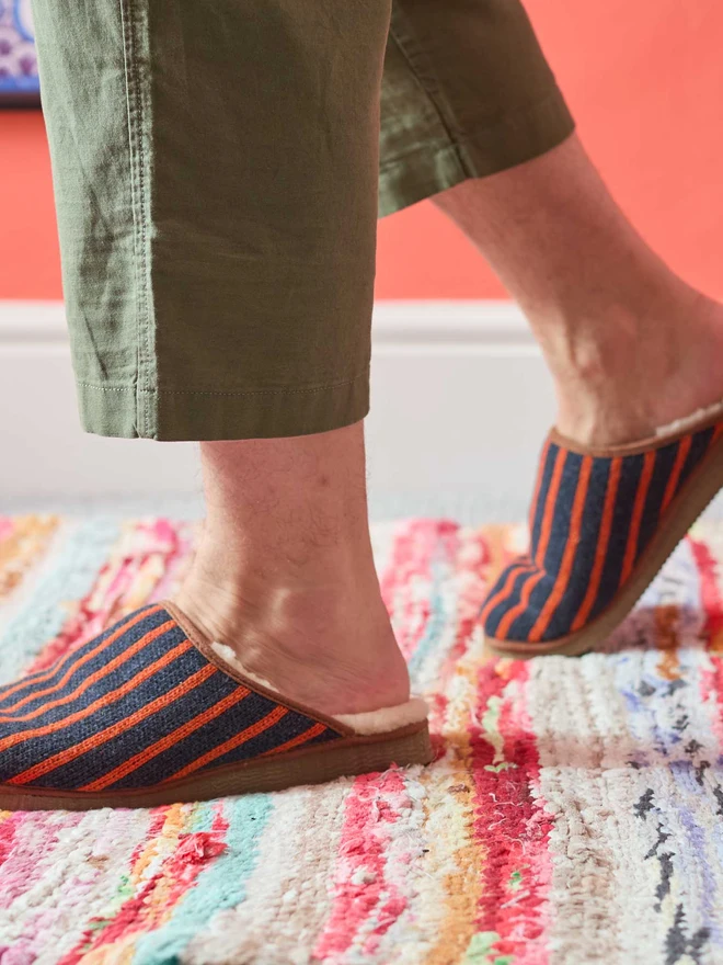 MAN WALKING IN NAVY BLUE STRIPED SLIPPERS IN FRONT OF A CORAL WALL