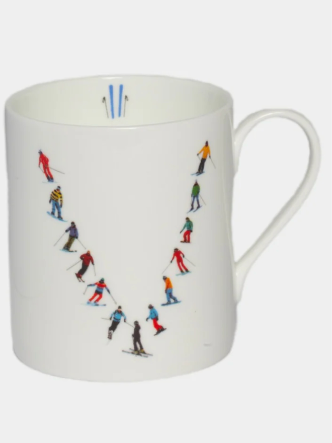 A simple white mug illustrated with a ‘V’ made of small, multicoloured skiers. The mug is set against a plain, white background.