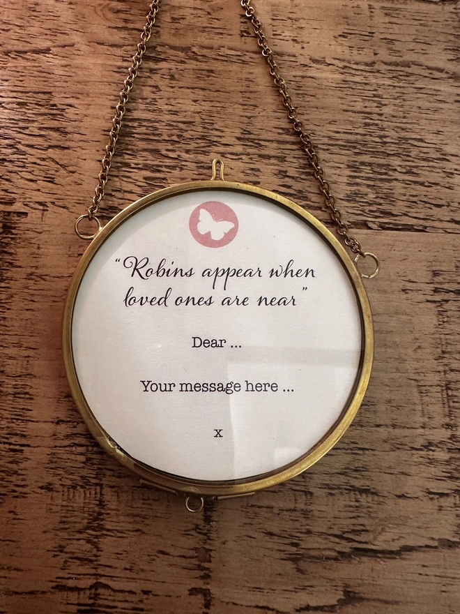 A photo showing the message 'Robins appear, when love ones are near" on the back of the circular, brass, hanging frame, with option to add personalised message.