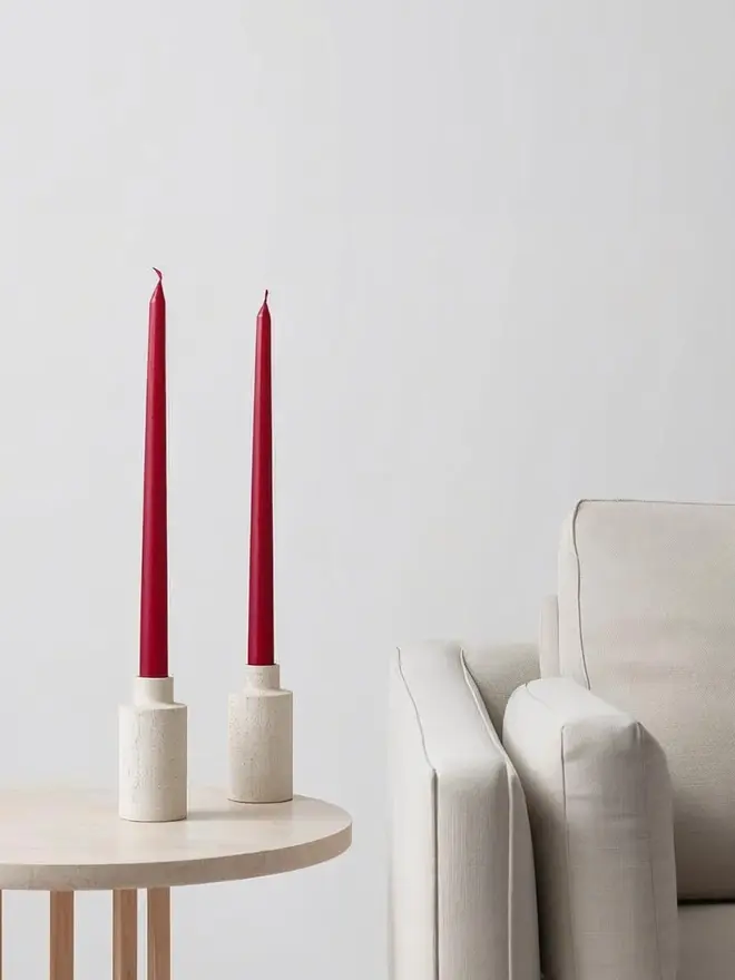 Two red dinner candles in candle holders on a table next to a sofa
