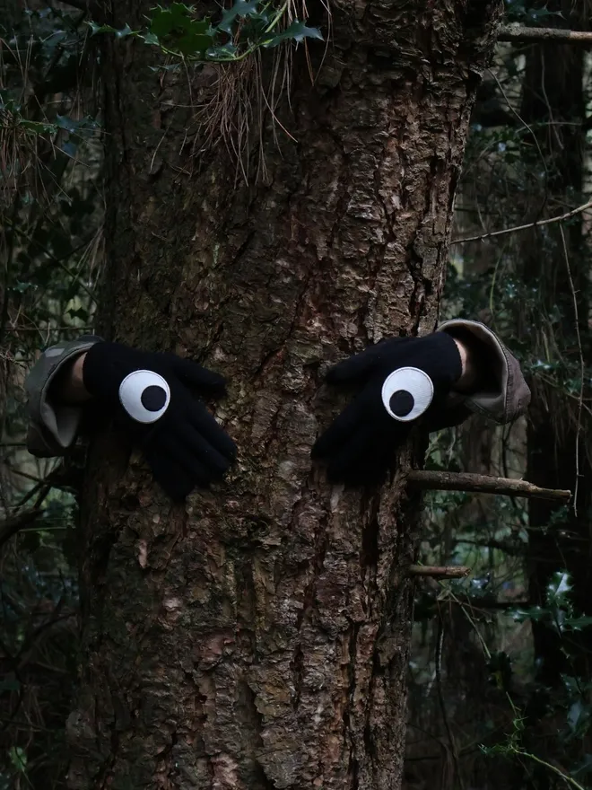 Googly eye iron on patches on black gloves in the woods