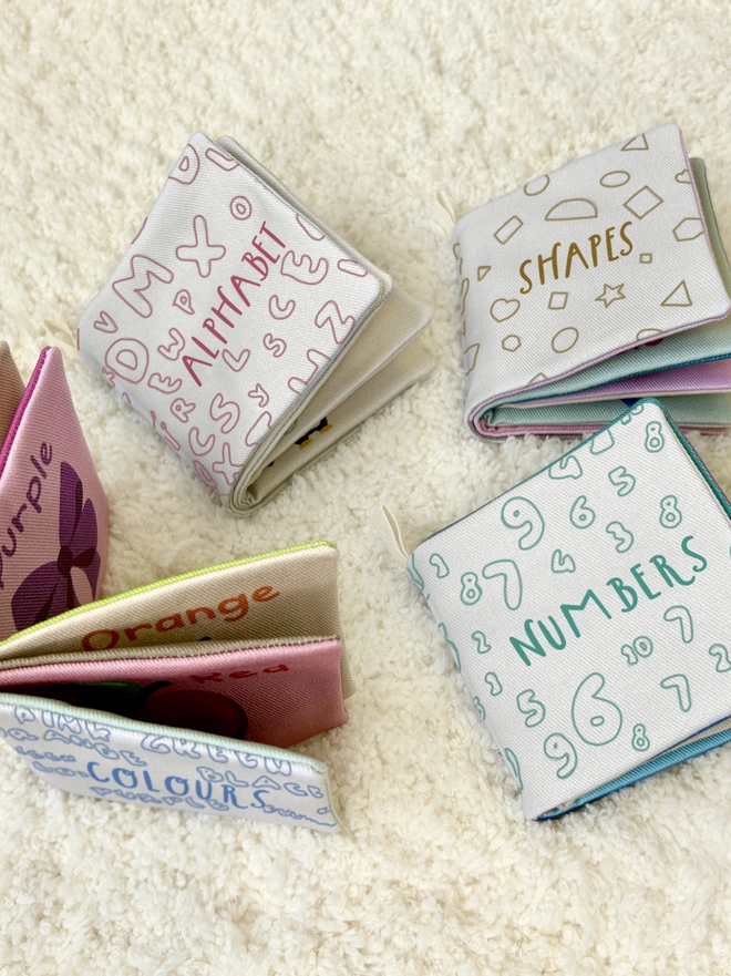 Picture of the 4 little softs books included in the book set with three of them laying on a rug closed and one standing open