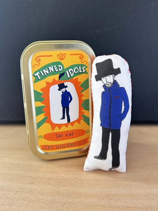 Mini fabric doll featuring illustration of Jamiroquai frontman, Jay Kay, in a tin.