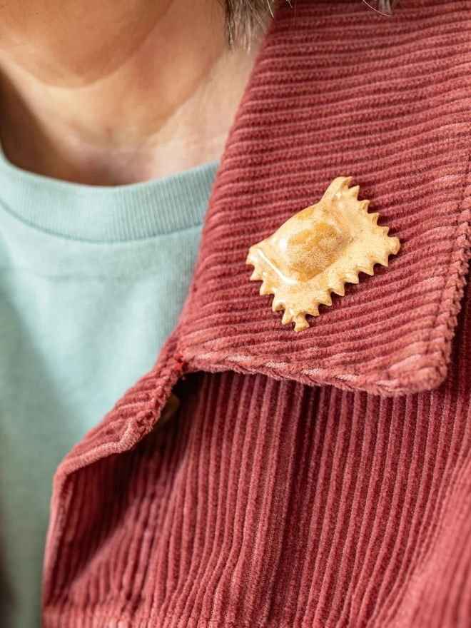 ceramic pasta pin badges. a ceramic ravioli badge photographed on a jacket.