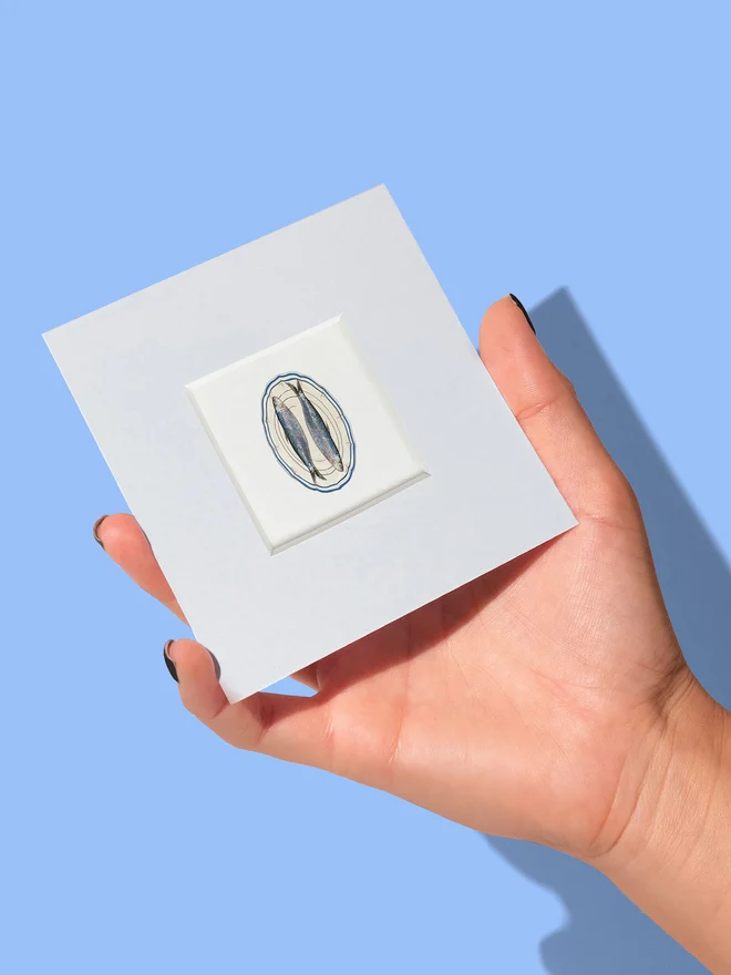 Hand holding a 4x4 mini pint showing the size of the Sardines on a Plate tiny print