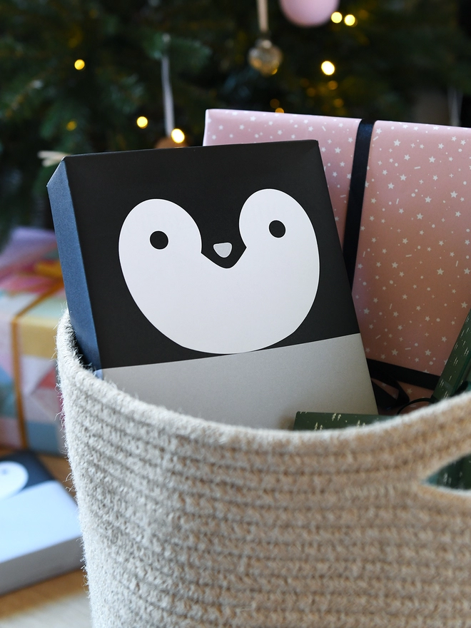 A gift wrapped in penguin wrapping paper is tucked into a woven basket with several other wrapped gifts.