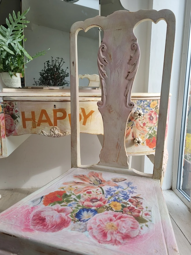 An antique kidney-shaped dressing table with chair and a trio of mirrors. Upcycled in cream and pale pink with decoupage florals in oranges and pinks. Text across the table read ‘flowers make me happy’ in the orange of the undercoat.