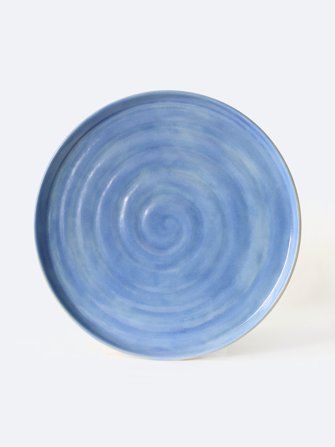 A handmade ceramic side plate in pacific blue glaze, photographed from the front against a plain white background, showing a natural concentric swirl texture from the wheel-throwing process