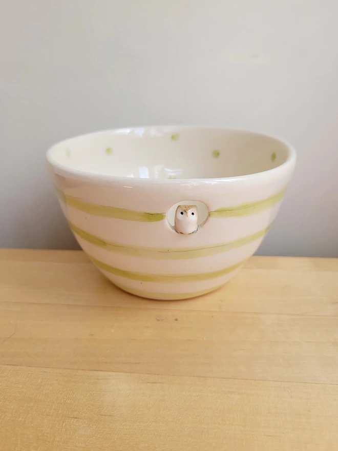 a pottery off white bowl with green spots and stripes and a miniature owl in a cut out hole