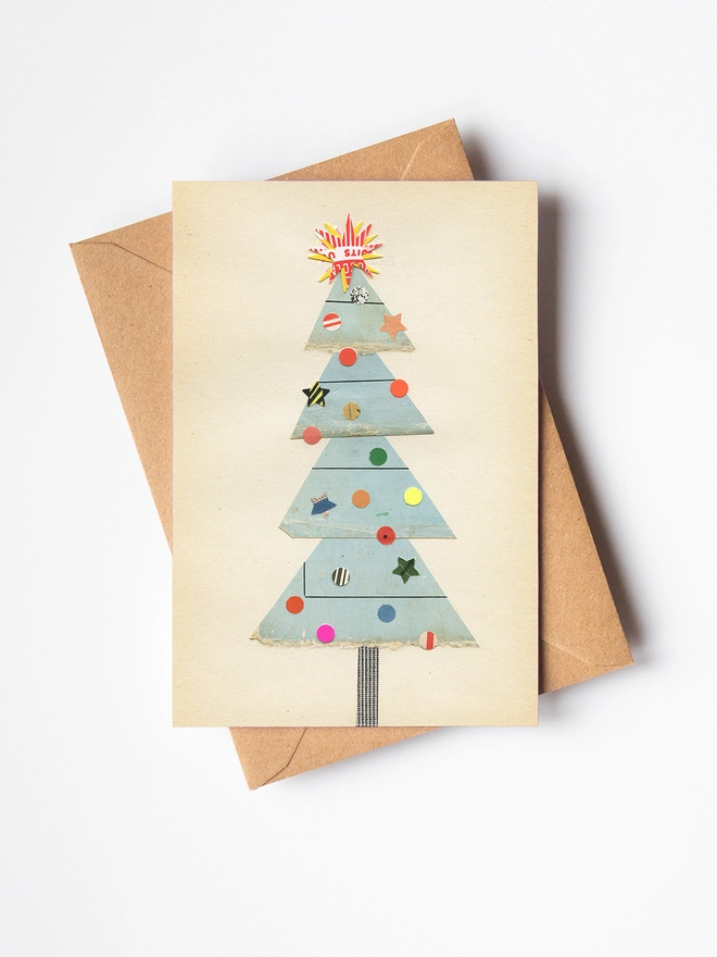 A charming Christmas card featuring a pale blue tree with a collection of eclectic decorations and a large star on top.