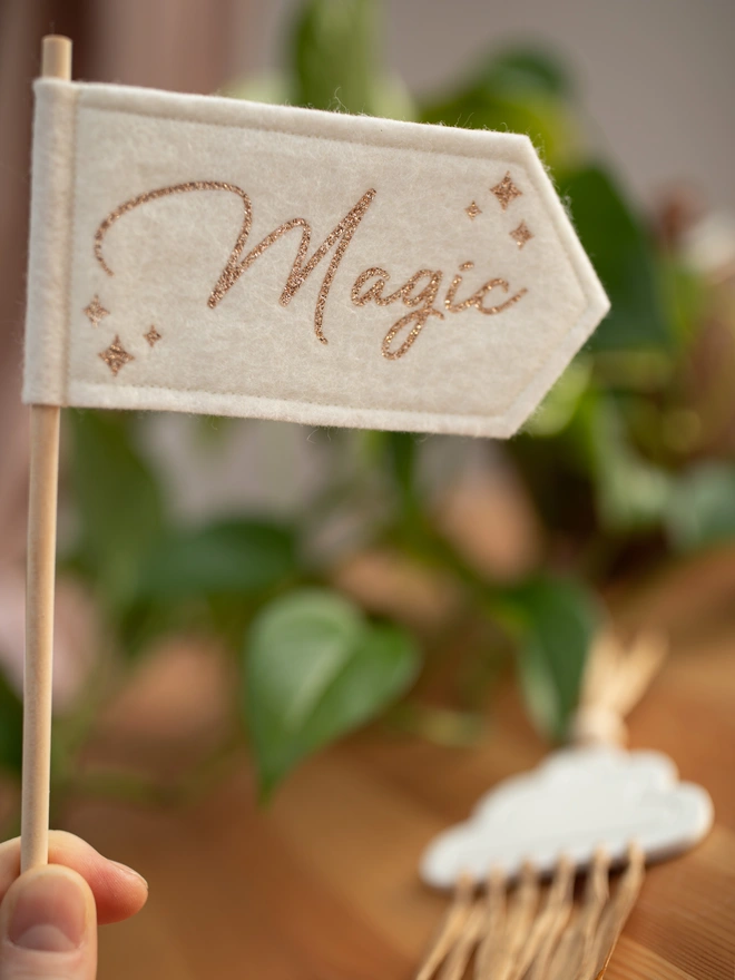 white handheld felt flag that has the word "magic" written on it it gold glitter
