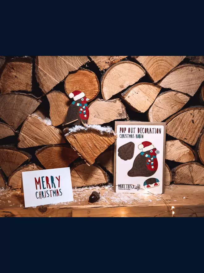 Robin Christmas decoration and Merry Christmas card on wooden logs with fairy lights in the background