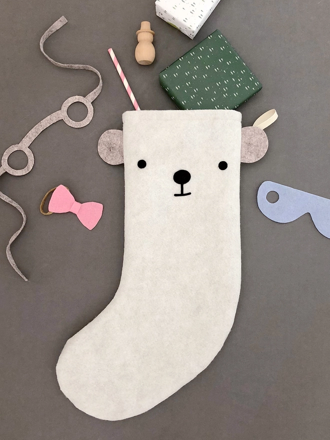 A handmade felt polar bear stocking lays on a grey surface with several gifts poking out from the top.