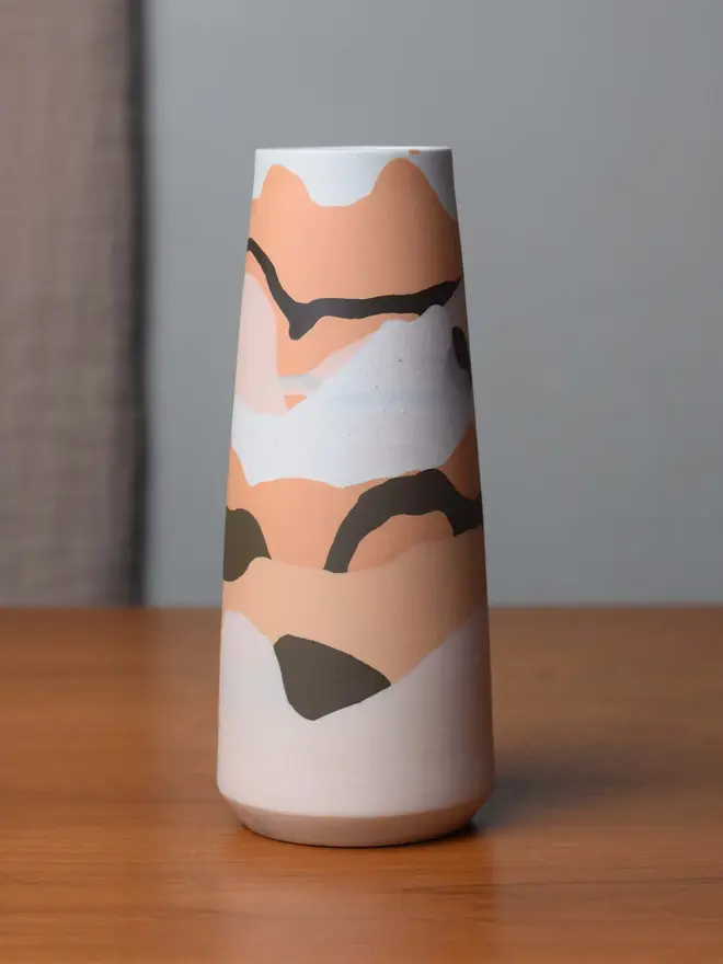 porcelain vase on table, vase has shades of orange, brown, and whites