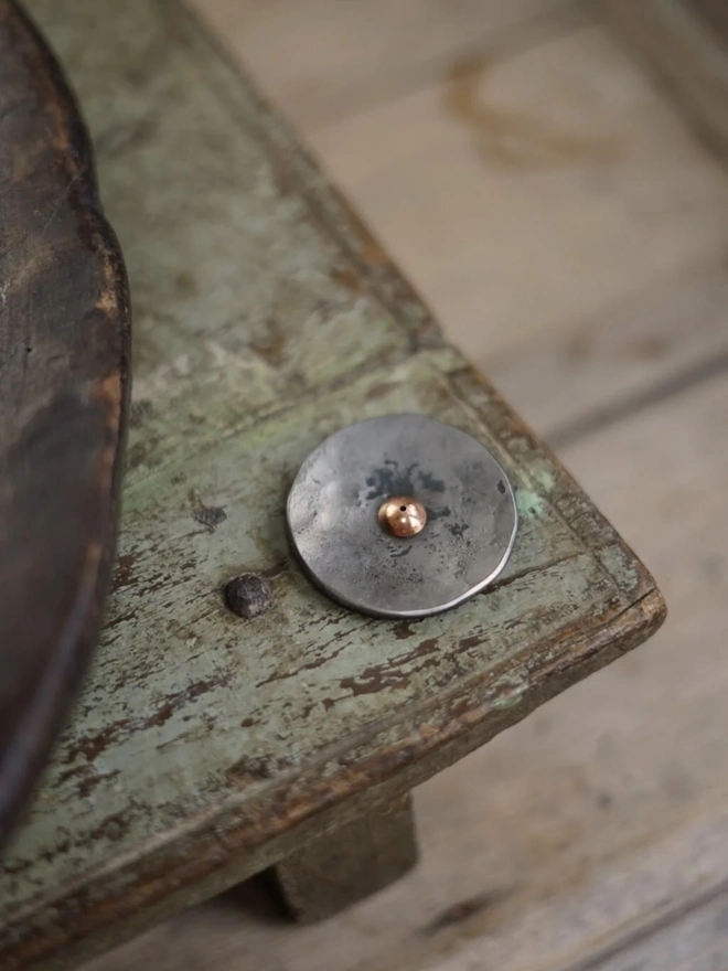 Copper And Steel Incense Holder, a metal incense holder sitting on a wooden surface in a workshop. 