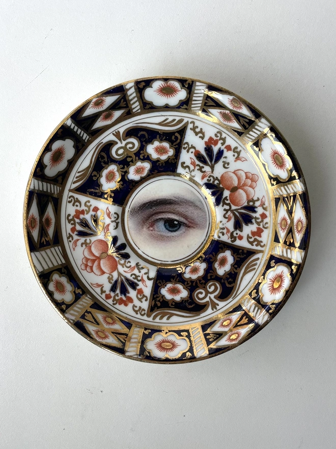 vintage plate with an ornate border, with a printed vintage illustration of an eye in the middle 