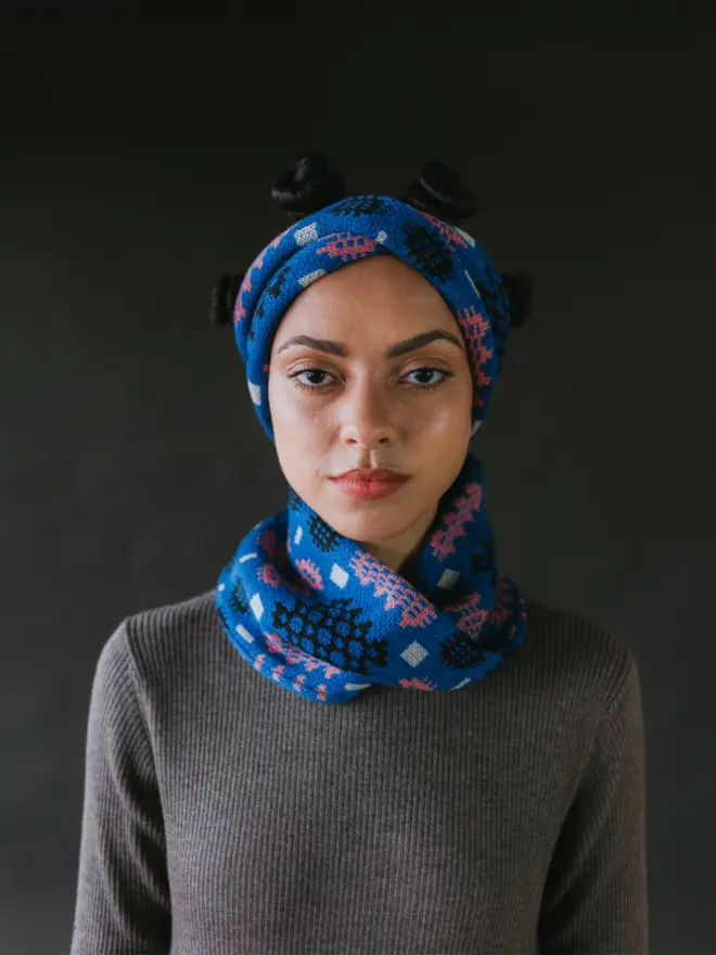 Model wearing pieces from MABLI's 'Carthen' collection, featuring the Carthen Wrap in the vibrant 'Klein blue/Rhosyn' colour-way. The design showcases bold, colourful patterns inspired by traditional Welsh blanket tapestry.