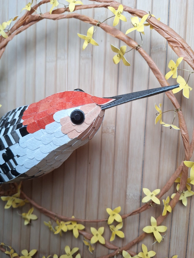 Close up of the face of the woodpecker sculpture, featuring a coral forehead of feather, white neck and peach cheeks and eye detail. The woodpecker has a long and pointy grey beak.