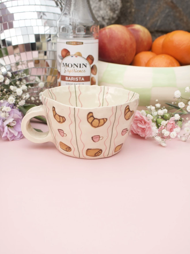 handmade stoneware mug decorated with handpainted croissants, coffee cups and pain au chocolat in a striped pattern