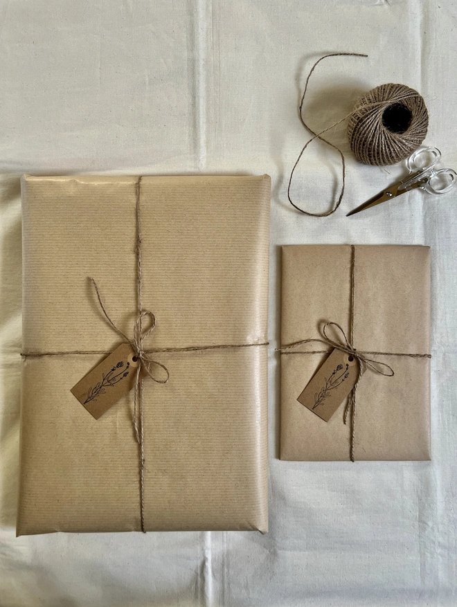 two different size artworks gift wrapped in brown paper with a hand stamped flower tag and brown string 