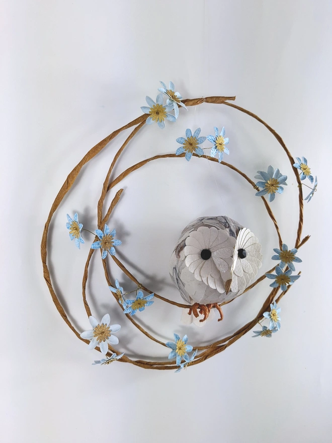 handmade paper sculpture of a barn owl baby, perched on a spring wreath of baby blue flowers