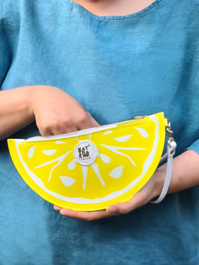 Juicy Leather Lemon Clutch Bag seen held by someone wearing a blue t-shirt.