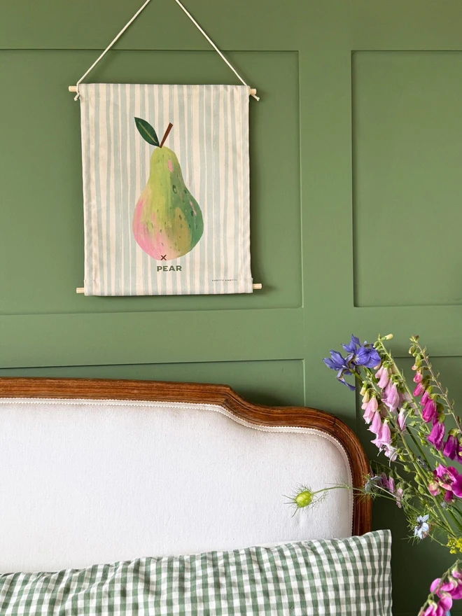 Cotton Pear Wall Hanging, hanging on a green wall. 