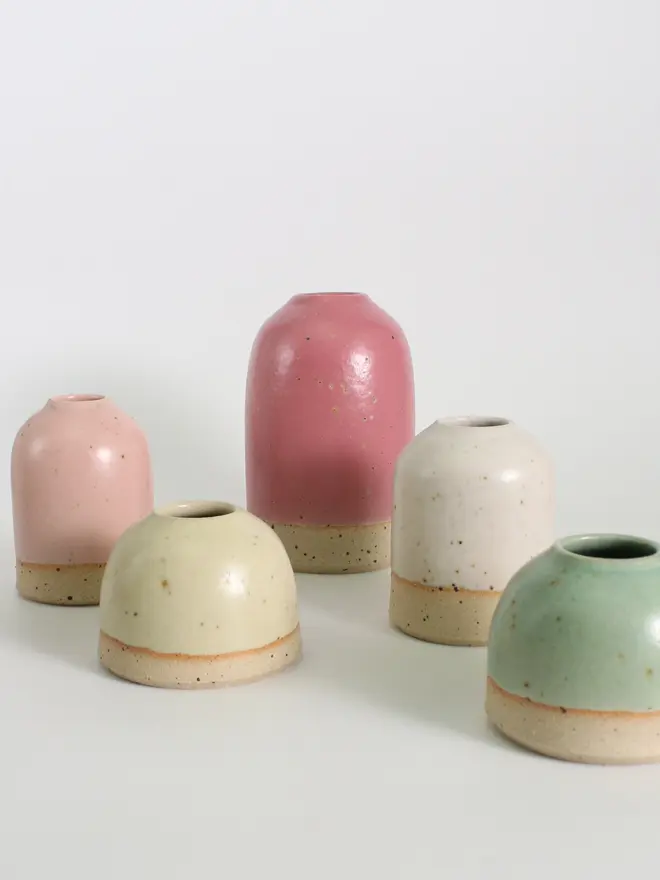 An arrangement of mini, small and medium vases against a white background. The image features pale yellow and mint green mini vases, off-white and pale pink small vases and a fuchsia medium vase.