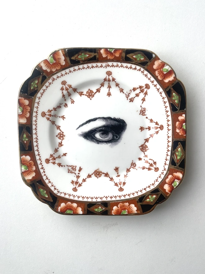 an ornate vintage plate with detailed border and in the centre an vintage illustration of an eye