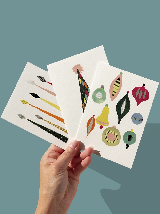 A set of three mid century inspired Christmas cards featuring festive candles, baubles and a decorated tree.