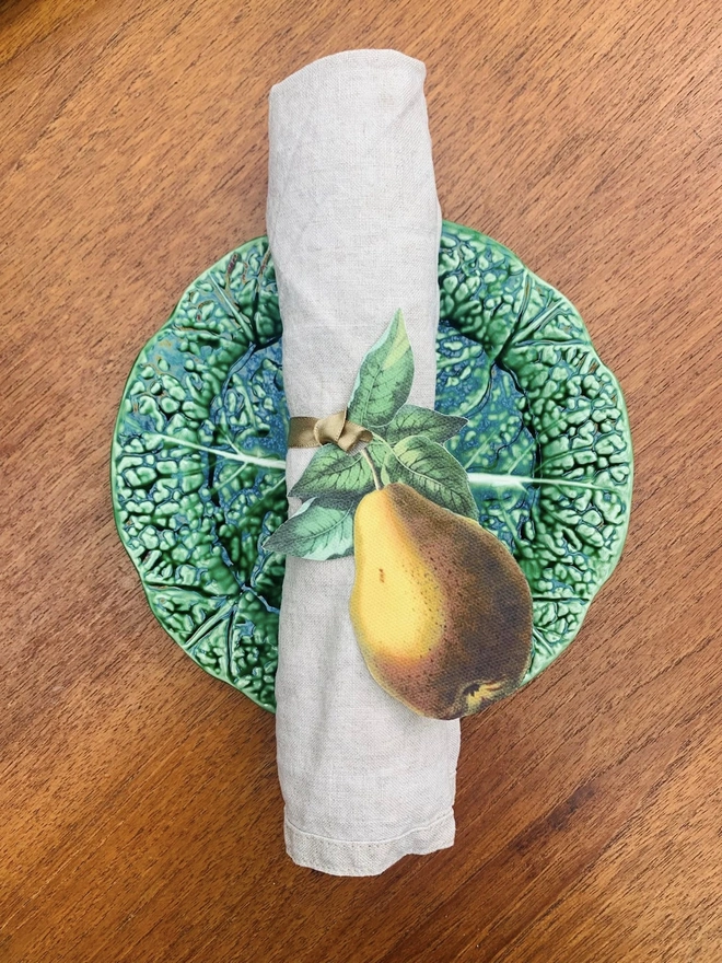 A golden pear napkin tie around a linen napkin on a cabbageware plate