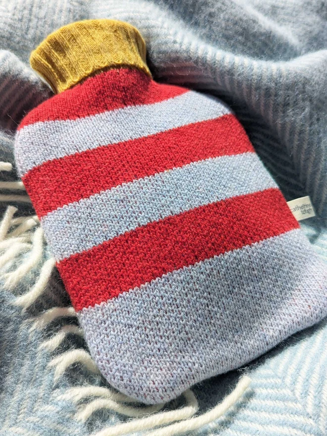 COLOURFUL HOT WATER BOTTLE COVER DISPLAYED ON A ON A BLANKET