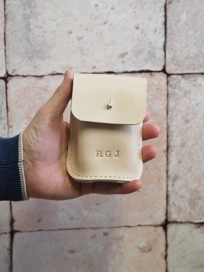 Personalised Leather Playing Card Holder, a natural cream coloured leather playing card case with 3 initials stamped on the front. Held in a mans hand.