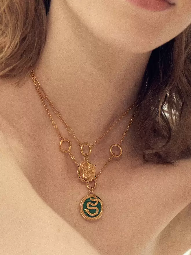 woman wearing two gold necklaces featuring a crossed arrows pendant and a malachite snake pendant.