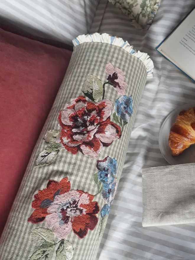 Close-up of colourful floral embroidery on a sage green gingham bolster cushion with gathered ruffle trim.