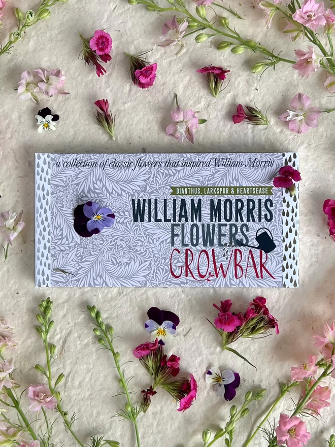 The William Morris Flowers Growbar laying on a background of purple and blue flowers. 