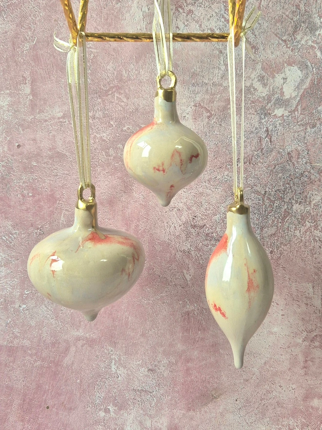 Ceramic christmas bauble decorations in a pearlescent glaze with white, cream and pink and gold, with silk ribbon and gold detailing. Photographed on a pearlescent serving dish with gold pears and christmas lights, gift, christmas, ceramics, pottery, christmas, decorations, christmas tree