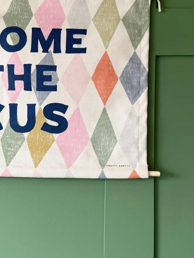 'Welcome To The Circus' Cotton Wall Hanging, hanging on a green wall. 