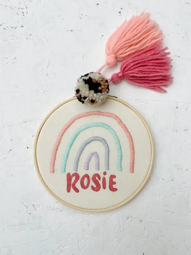 personalised name and rainbow embroidered hoop. cotton hoop embroidered with the name rosie and a blue and pink rainbow.